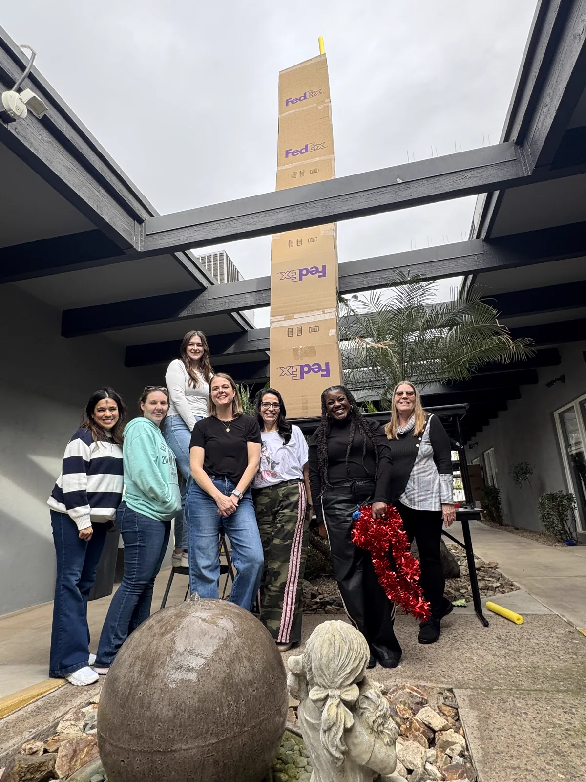 A team standing together beneath a tall structure they built from cardboard boxes.